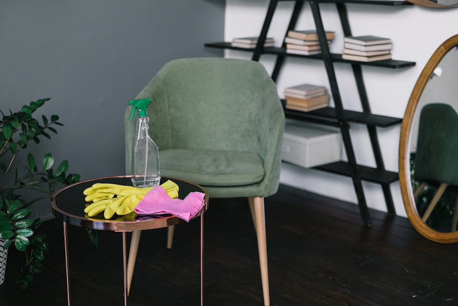 A professional cleaner from South Hackney Carpet Cleaners is performing surface cleaning on a wooden dining table in a well-lit, modern living room. She is wearing a black uniform with gloves and is u
